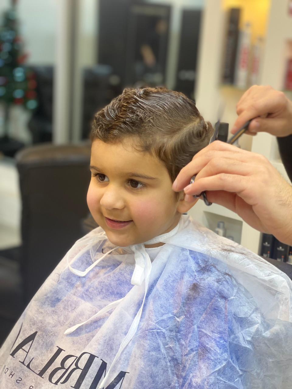 A smiling young boy getting a haircut in a Mr. Black cape