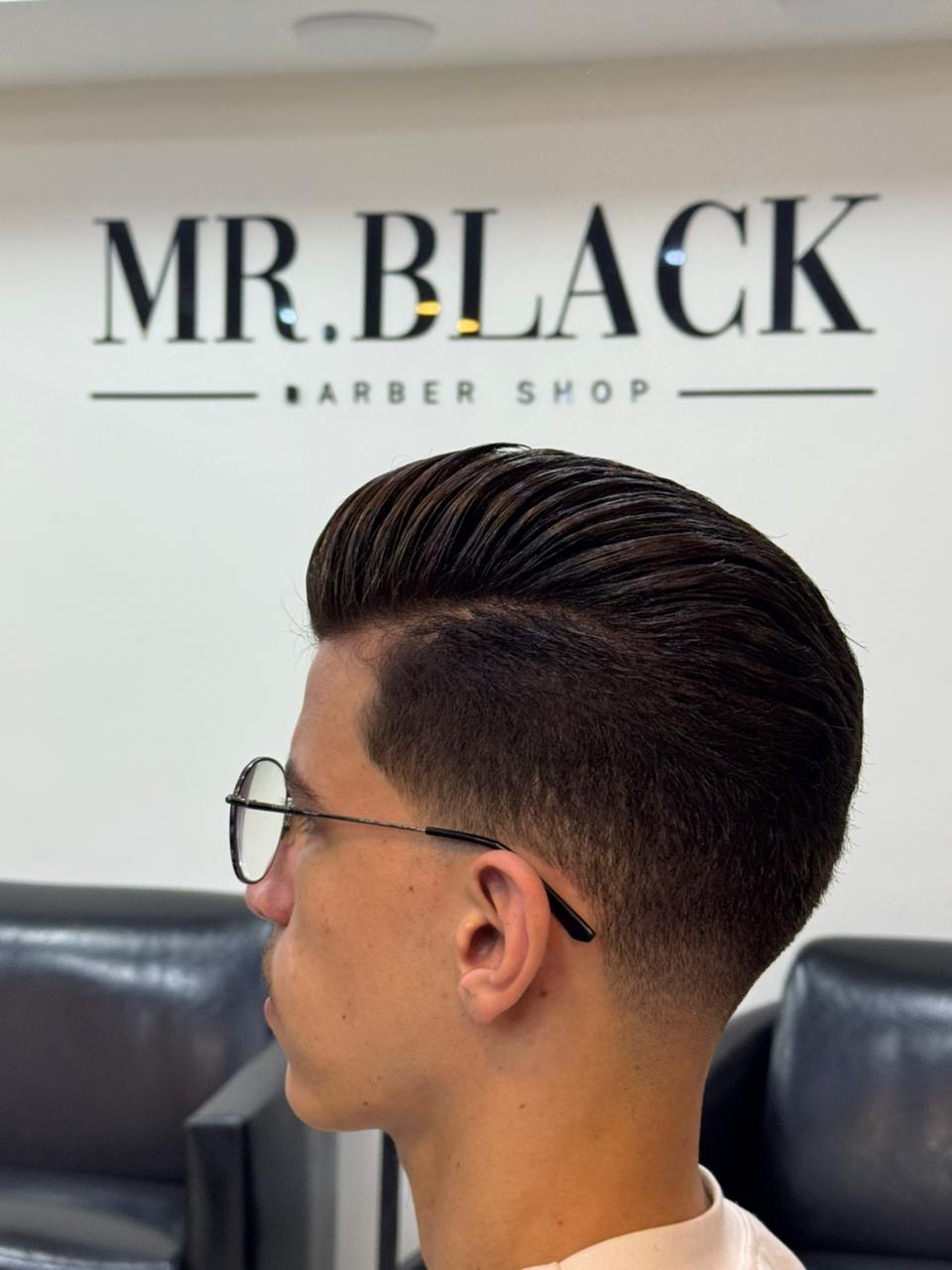 Finished slicked-back fade in front of the Mr. Black Barber Shop wall logo
